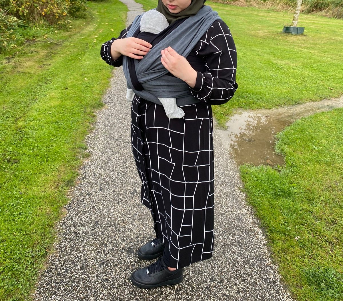 Feride draagt haar baby op de buik in een grijze geweven draagdoek op een grindpad