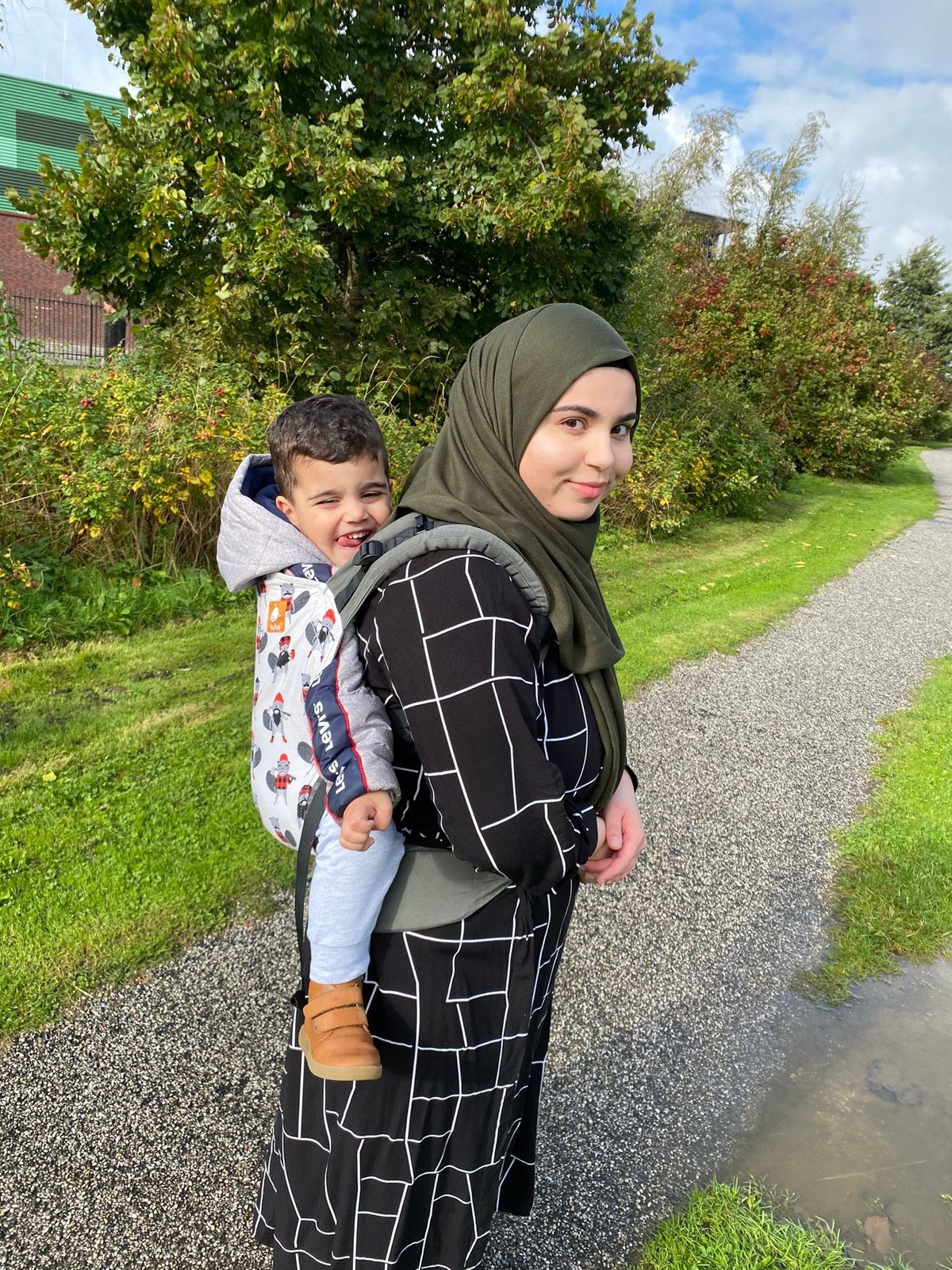 Feride draagt een lachende peuter op haar rug op een wandelpad