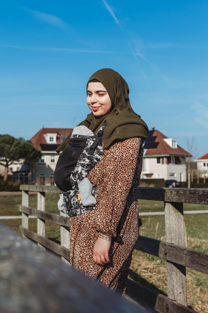 Feride Kiliçaslan staat bij een houten hek en draagt haar kindje in een draagzak